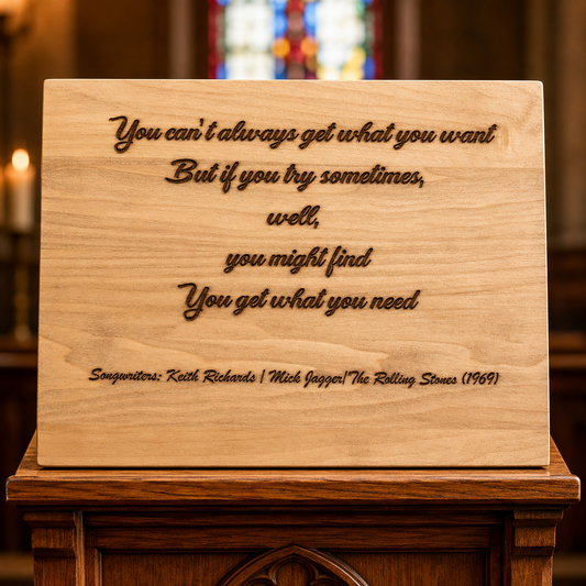 A rectangular wooden plaque engraved with a motivational quote and songwriters' names, displayed on a dark wooden altar stand in a church setting with blurred stained glass and candles in the background.